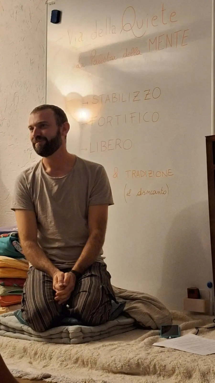 Eros sorridente, in ginocchio davanti alla lavagna su cui è scritto «Via della Quiete, la palestra della Mente»