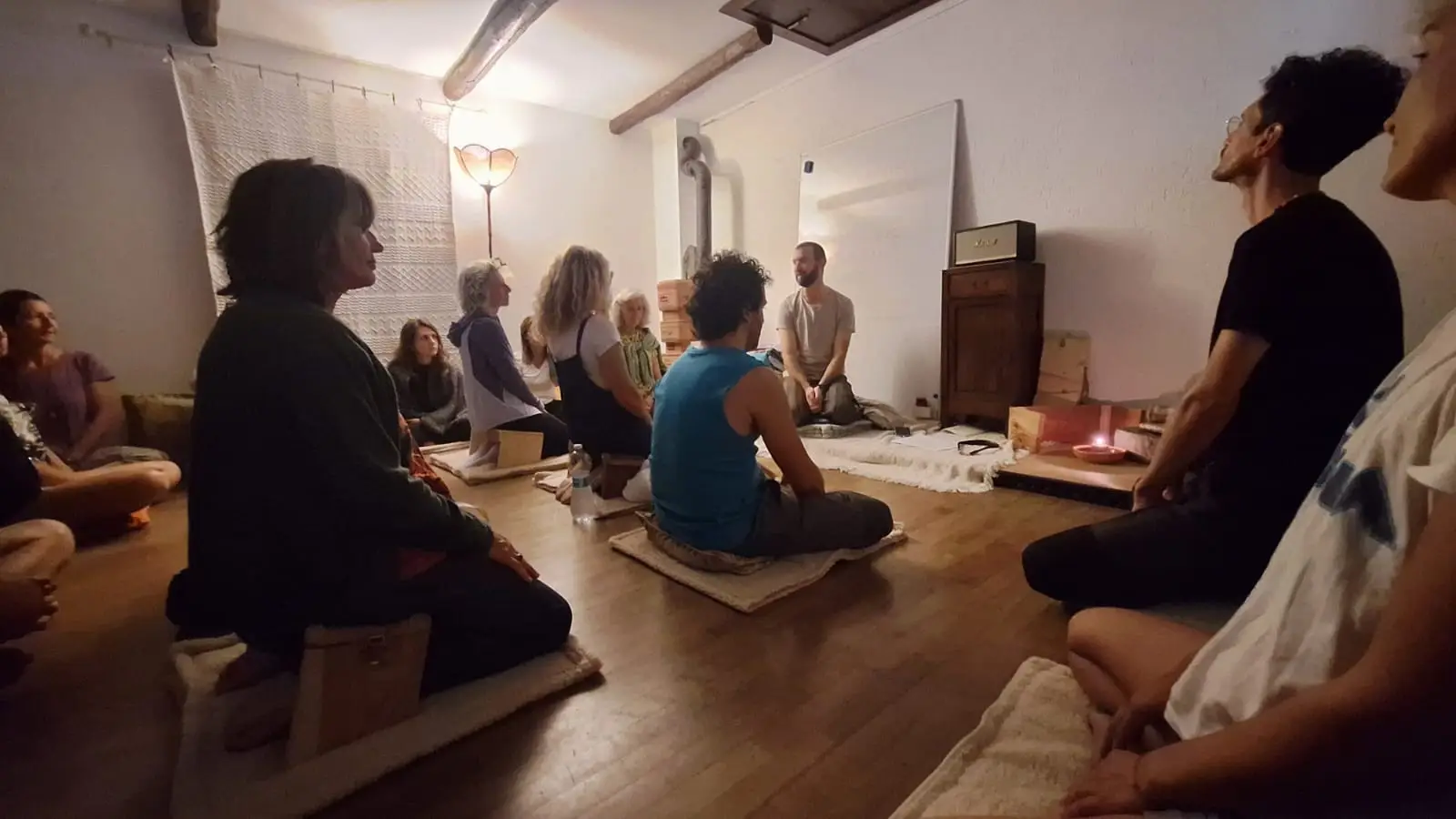Un incontro di Via della Quiete: le persone sedute in cerchio su cuscini e panchette, Eros che guida la pratica