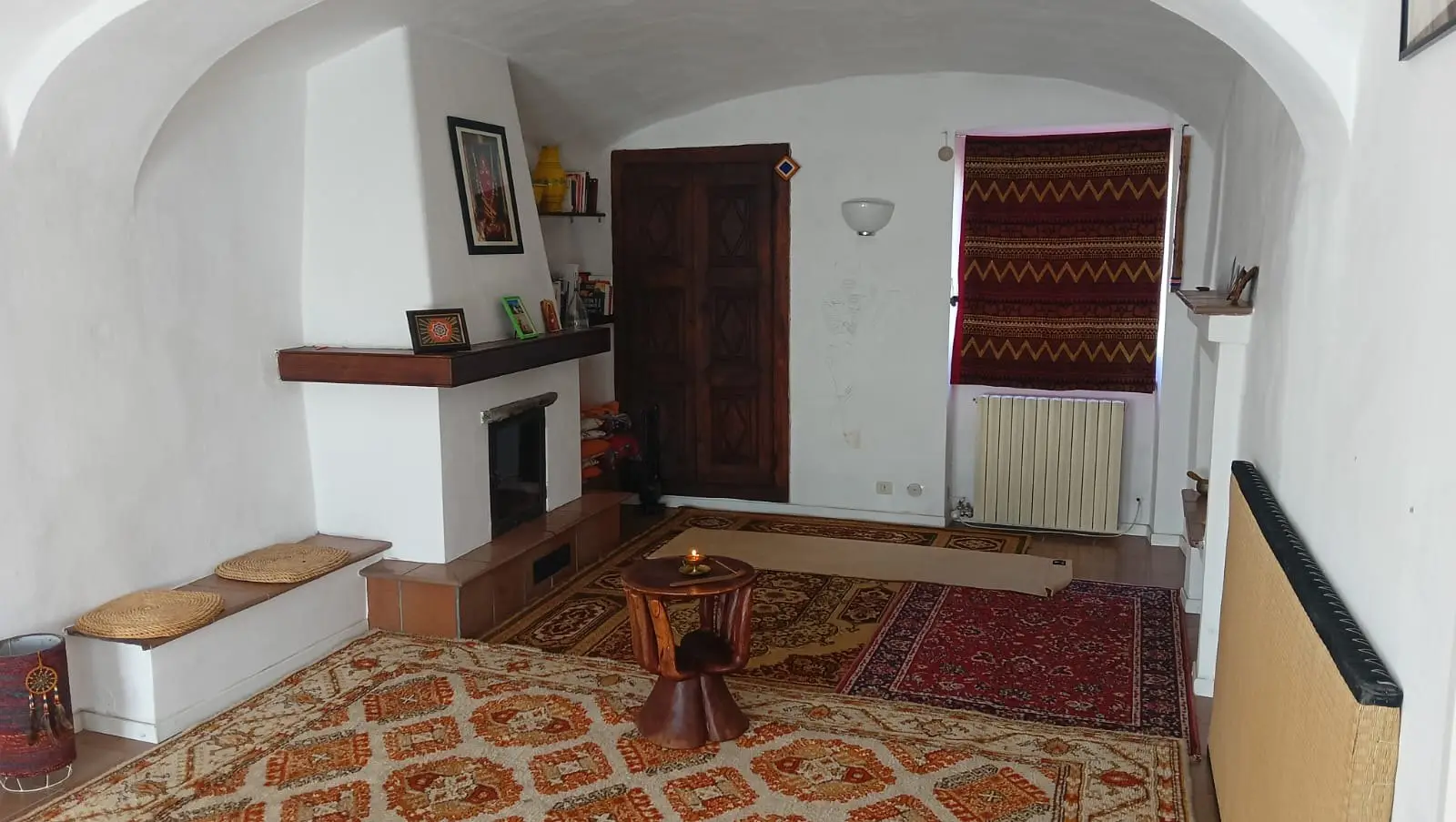 La sala di meditazione di Corso Bisalta 169 a Boves la sera: le volte, i tappeti sovrapposti e il camino acceso