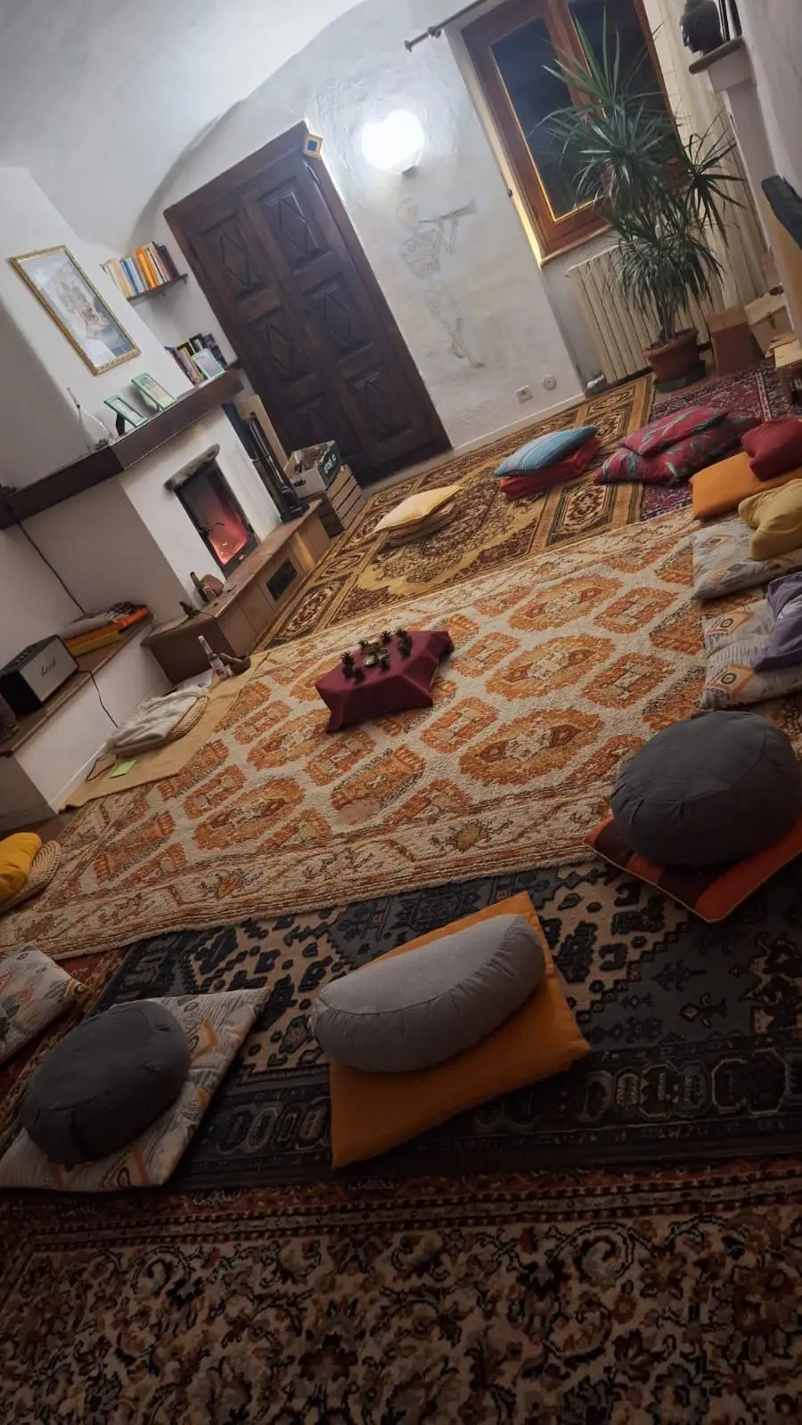 La sala di meditazione di Boves pronta per il Primo Passo: cuscini sui tappeti, il camino acceso in fondo