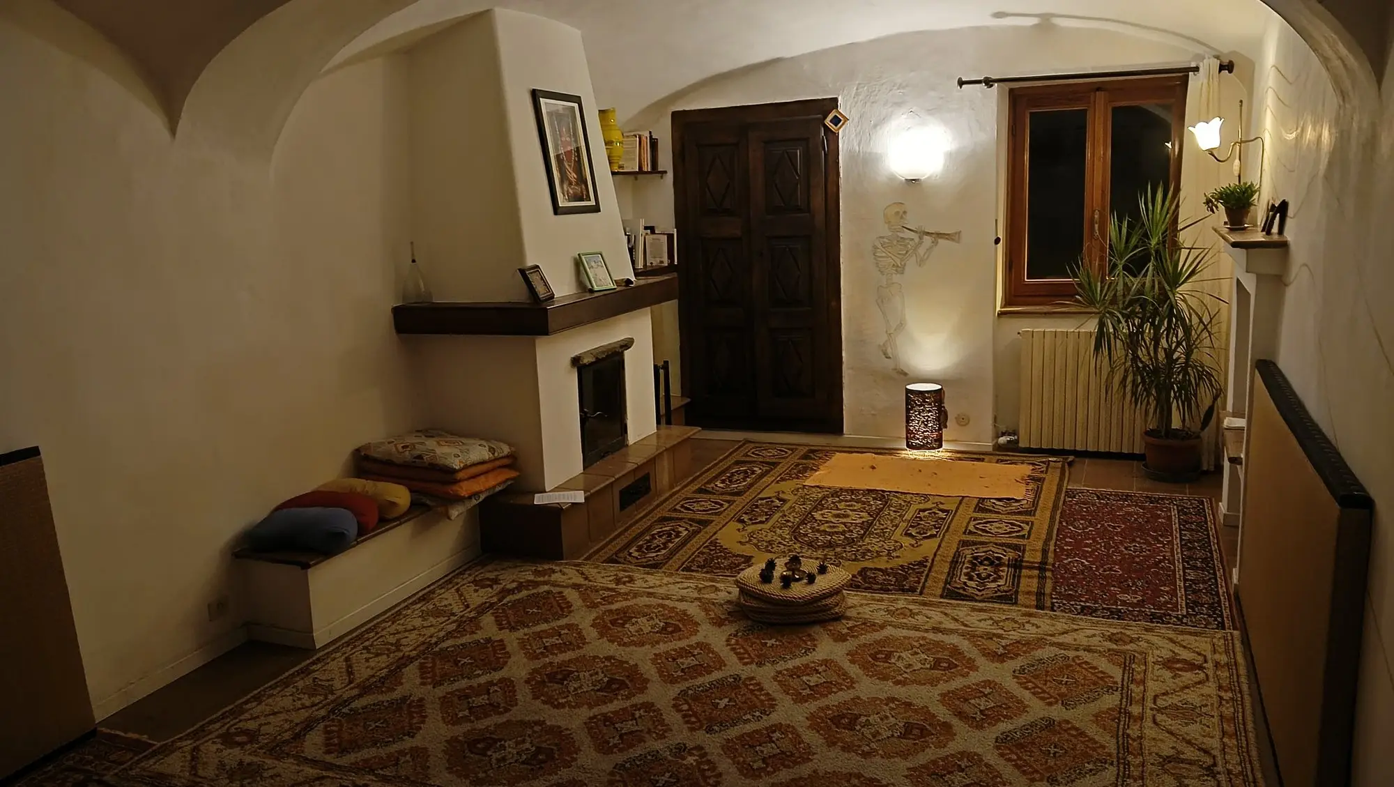 La porta di legno della Sala Tappeti sotto le volte, con i tappeti sovrapposti e i cuscini accanto al camino